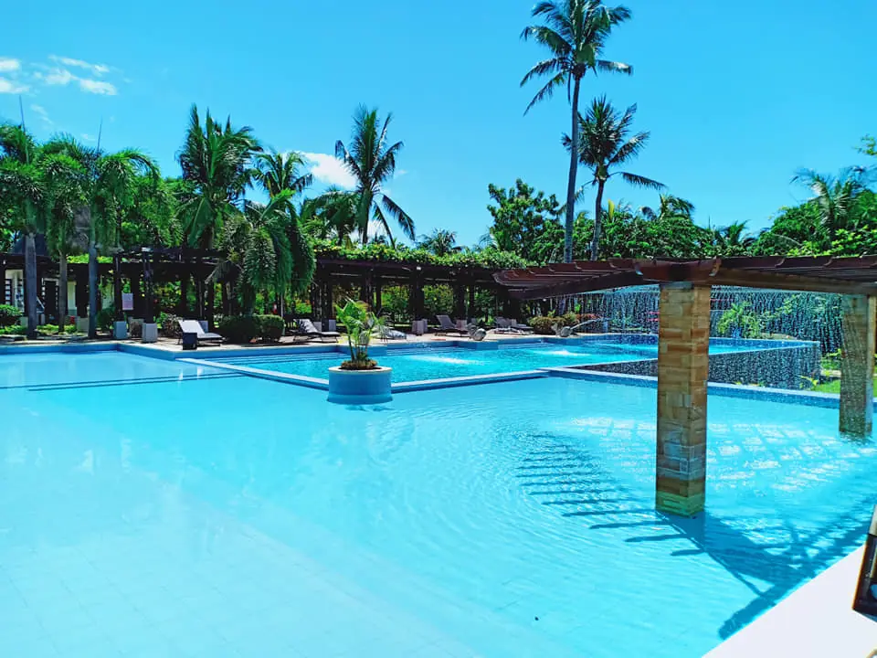 Outdoor swimming pool with a water curtain feature, pergola, lounge chairs and coconut palms
