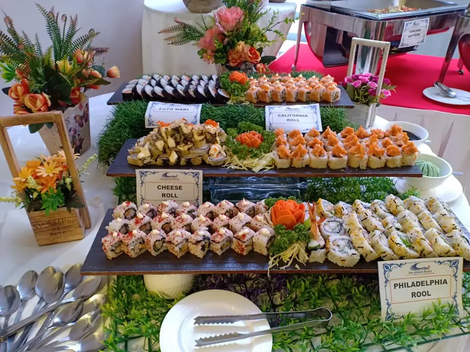 Buffet table of sushi rolls on wooden boards with labels reading Futo Maki, California Roll, Cheese Roll