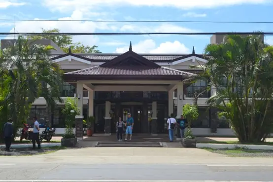 Front of a two storey building with a brown tiled pavilion roof, palms and parked motorcycles