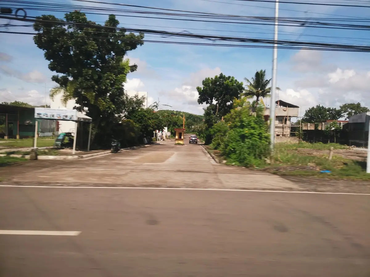 Subdivision entrance road with a guardhouse, seen from across the highway