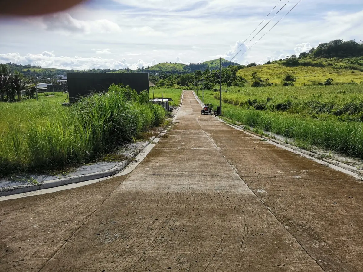 Concrete road running uphill between tall grass, green hills ahead and a parked motorcycle